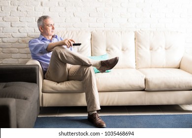 Middle Aged Man Sitting On Sofa Changing The Channels Of Television With Remote Control While Watching Tv At Home