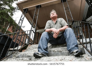 Middle aged man sitting on the steps of a house in the inner city, focus on face