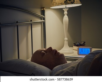 Middle Aged Man Sleeping In Bed, An Alarm Clock On The Night Table