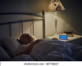 Middle Aged Man Sleeping In Bed, An Alarm Clock On The Night Table