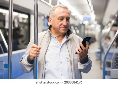 Middle aged man with smartphone in hand standing in subway car and holding handrail.