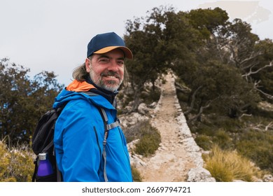 Middle aged man smiling while hiking on a forest mountain path. Concept of outdoor lifestyle, nature enjoyment, active aging.