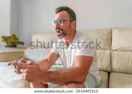 Middle Aged Man Smiling While Playing Video Games on the Sofa at Home