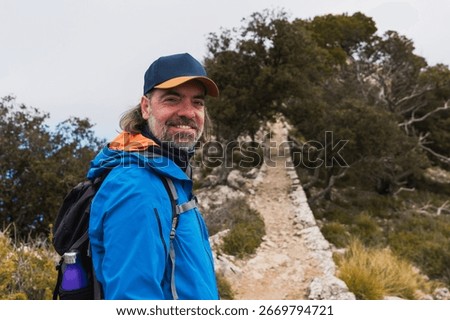 Middle aged man smiling while hiking on a forest mountain path. Concept of outdoor lifestyle, nature enjoyment, active aging.
