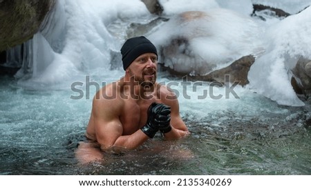 middle aged man with swimsuit, fur hat and a neoprene gloves is hardening the body  in cold river wather in the winter. Good immunity is protection against many diseases. 