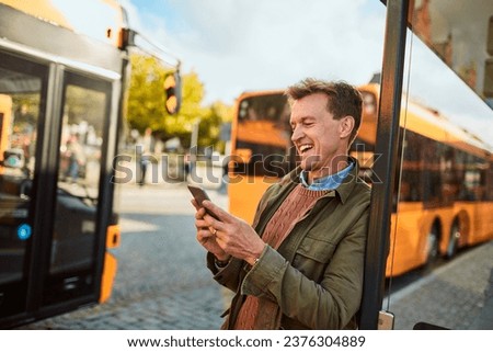 Middle aged man using his smartphone at the bus stop
