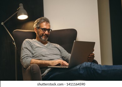 Middle Aged Man Using Laptop Relaxed In Sofa In His Home