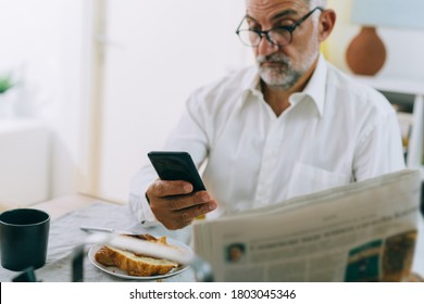 middle aged man using mobile phone while having breakfast at home
