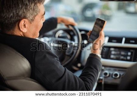 Middle aged man using a smart phone while driving a car