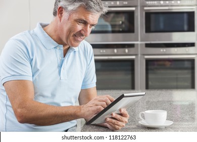 Middle Aged Man Using Tablet Computer At Home In The Kitchen Drinking Coffee Or Tea