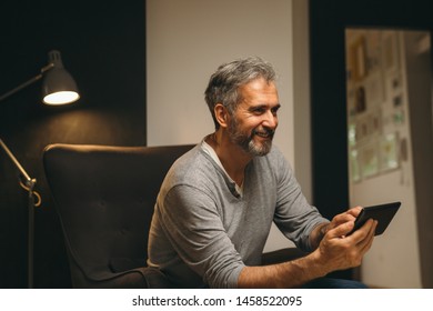 middle aged man using tablet while sitting in sofa at his home