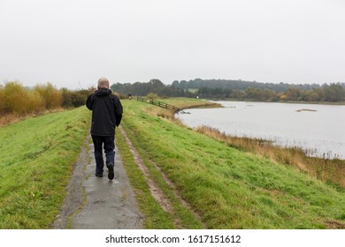 A Middle Aged Man Walking Along A River Path While Talking On His Mobile Phone