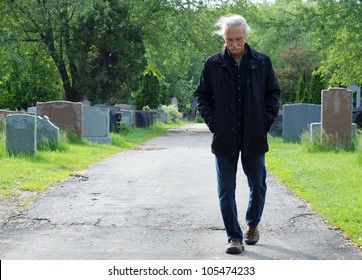 Middle Aged Man Walking In Cemetery With Head Down.