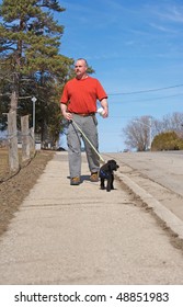 A Middle Aged Man Walking His Dog On The First Warm Day In Spring.