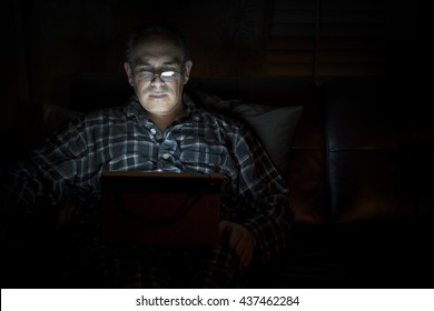 Middle aged man wearing pajamas reading tablet at night in bed with serious and worried expression, copy space - Powered by Shutterstock