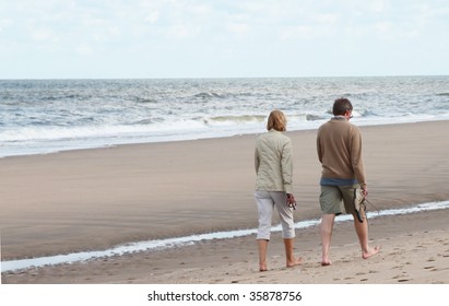 Middle Aged Man And Woman Taking A Walk On The Beach.