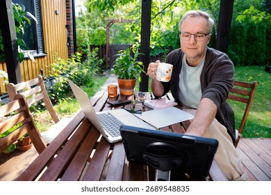 Middle aged man working remotely on laptop at cozy sunny patio, digital nomad lifestyle, outdoor home office, freelance and productivity concept