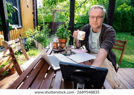 Middle aged man working remotely on laptop at cozy sunny patio, digital nomad lifestyle, outdoor home office, freelance and productivity concept