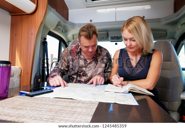 Middle aged married couple talking about future\
adventure planning route looking at map sitting inside of\
recreational vehicle motor home trailer. Active lifestyle,\
traveling by motor vehicle\
concept