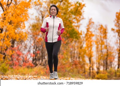 Middle Aged Mature Asian Woman Running Healthy Lifestyle Chinese Lady Jogging In Fall Park In Her 50s. Middle Age Runner Outdoor Living In Autumn City Forest Happy On Weight Loss Fitness Program.