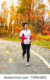 Middle Aged Mature Asian Woman Running Healthy Lifestyle Chinese Lady Run Jogging In Fall Park In Her 50s. Middle Age Runner Outdoor Living In Autumn City Forest Happy On Weight Loss Fitness Program.