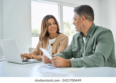 Middle aged mature couple using laptop counting taxes with receipts to save money at home. Older man and woman paying bills online planning financial budget savings calculating payments sit at table. - Powered by Shutterstock