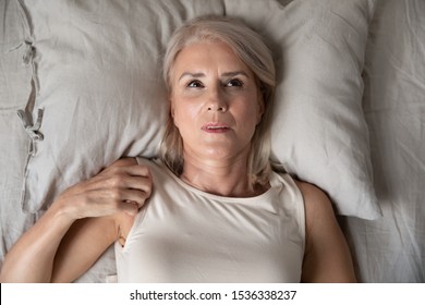 Middle aged mature woman insomniac lying awake in bed looking up trying to sleep, unhappy old senior lady feel disturbed frustrated suffer from insomnia concept uncomfortable bad mattress, top view