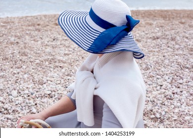 Middle Aged Mature Woman Posing On The Beach In The Sea. Wearing Grey Dress, Straw Hat And Bag