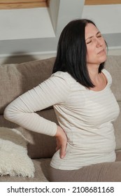  Middle aged mature woman suffering from backache and flank pain at home. Muscle problems, kidney stones or gallbladder disease. Symptoms of  desease or unhealthy lifestyle.                           