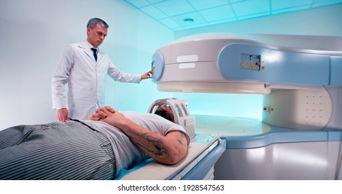 Middle aged medical practitioner releasing bearded man from MRI machine and taking off coil after brain scanning procedure in modern hospital