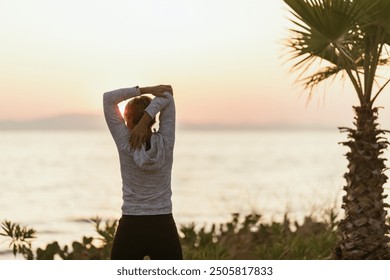 Middle aged muscular woman stretching arms above her head in a sunrise, near a beach during summer holiday. - Powered by Shutterstock