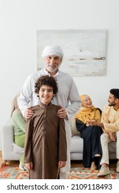 middle aged muslim man hugging shoulder of arabian grandson near multiethnic family on blurred background