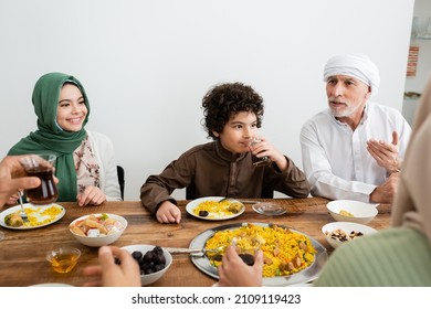 middle aged muslim man pointing with hand during dinner with interracial grandchildren