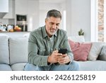 Middle aged old man using smartphone relaxing on couch at home. Happy senior mature male user holding cellphone browsing internet, texting messages on mobile cell phone technology sitting on sofa.