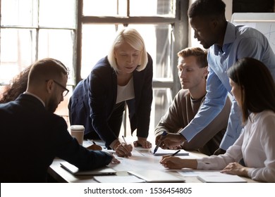 Middle Aged Older Female Leader Help Diverse Executive Team People In Paperwork Analysis At Group Briefing, Serious Focused Multiracial Employees Work On Project Plan Together At Office Meeting Table