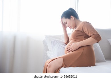 Middle Aged Pregnant Woman Sitting On Bed,having Headache From Hypertension,high Blood Pressure.