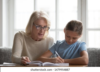 Middle aged private tutor in glasses helping to school child with homework explains educational material sit together on sofa, apprentice girl writing down make task having lesson at home with teacher - Powered by Shutterstock