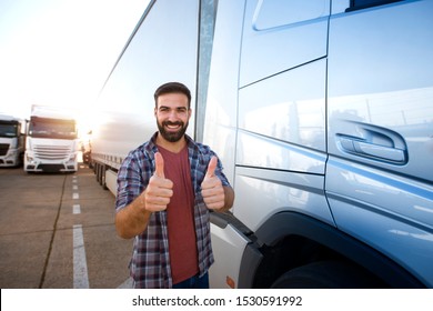 Middle Aged Professional Trucker Holding Thumbs Up And Standing By His Truck. Happy Truck Driver. Transportation Services.