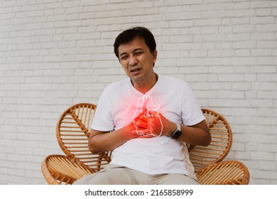 Middle aged, senior Asian man with sudden onset of heart disease showing pain heart muscle leaks tired and suffocating sits on a wooden chair in agony : Myocardial infarction (Heart Attack)