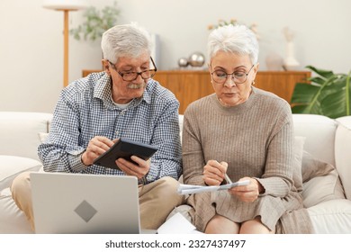 Middle aged senior couple sit with laptop and paper document. Older mature man woman reading paper bill pay online at home managing bank finances calculating taxes planning loan debt pension payment - Powered by Shutterstock