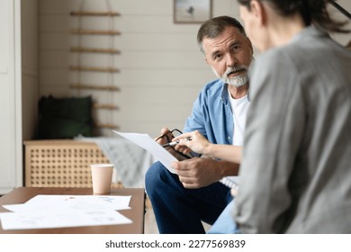 Middle aged senior old couple holding documents reading paper bills paying bank loan online, calculating pension fees, payments, taxes, planning family retirement money finances at home.