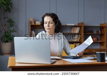 Middle aged senior woman sit with laptop and paper document. Pensive older mature lady reading paper bill pay online at home managing bank finances calculating taxes planning loan debt pension payment