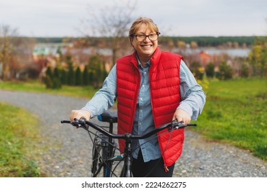 Middle aged smiling mature woman holdingt a bike with her hands on the grass on a green field. Summer or Autumn Country Vacation and Adventure Concept - Powered by Shutterstock