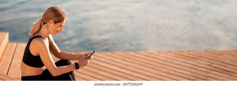 Middle Aged Sporty Woman Using Smartphone While Relaxing After Training Outdoors, Smiling Athletic Lady Messaging On Mobile Phone While Resting On Wooden Pier Near River, Copy Space - Powered by Shutterstock