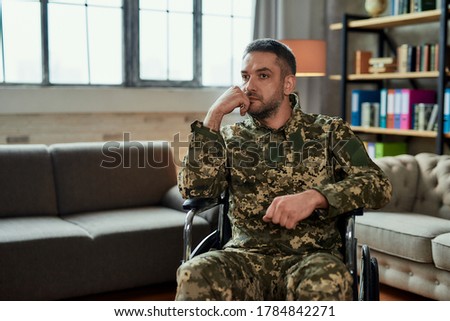 Middle aged thoughtful military man in a wheelchair looking away during therapy session. Disabled soldier suffering from depression, psychological trauma. PTSD concept. Horizontal shot