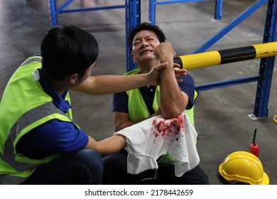 Middle Aged Warehouse Asian Worker Man Had Elbow Accident Sitting On The Floor In Warehouse Logistics Distribution Center. Safety Colleague Team Helping Him From Injury. First Aid Training Concept.
