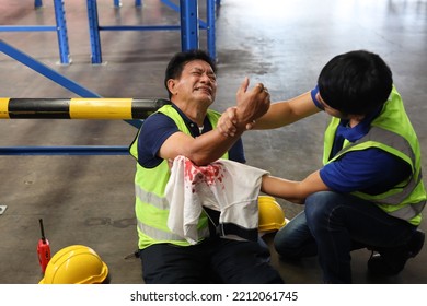 Middle Aged Warehouse Asian Worker Man Had Elbow Accident Sitting On The Floor In Warehouse Logistics Distribution Center. Safety Colleague Team Helping Him From Injury. First Aid Training Concept.