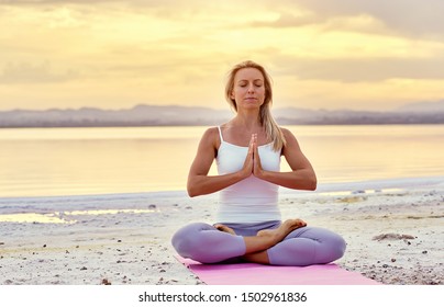 Middle aged woman in activewear make namaste gesture sitting in lotus position on beach near sea during sunset or sunrise closed eyes do meditation on nature, balance harmony healthy lifestyle concept - Powered by Shutterstock