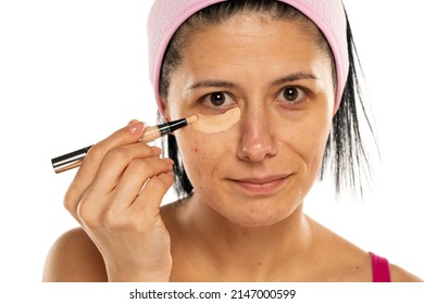 Middle aged woman apply concealer under the eye on a white background.