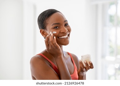 Middle aged woman applying hydrating moisturizer on her face, daily routine skin care. Smiling middle aged african woman holding little jar of skin cream and applying lotion on cheek, anti-aging cream - Shutterstock ID 2126926478